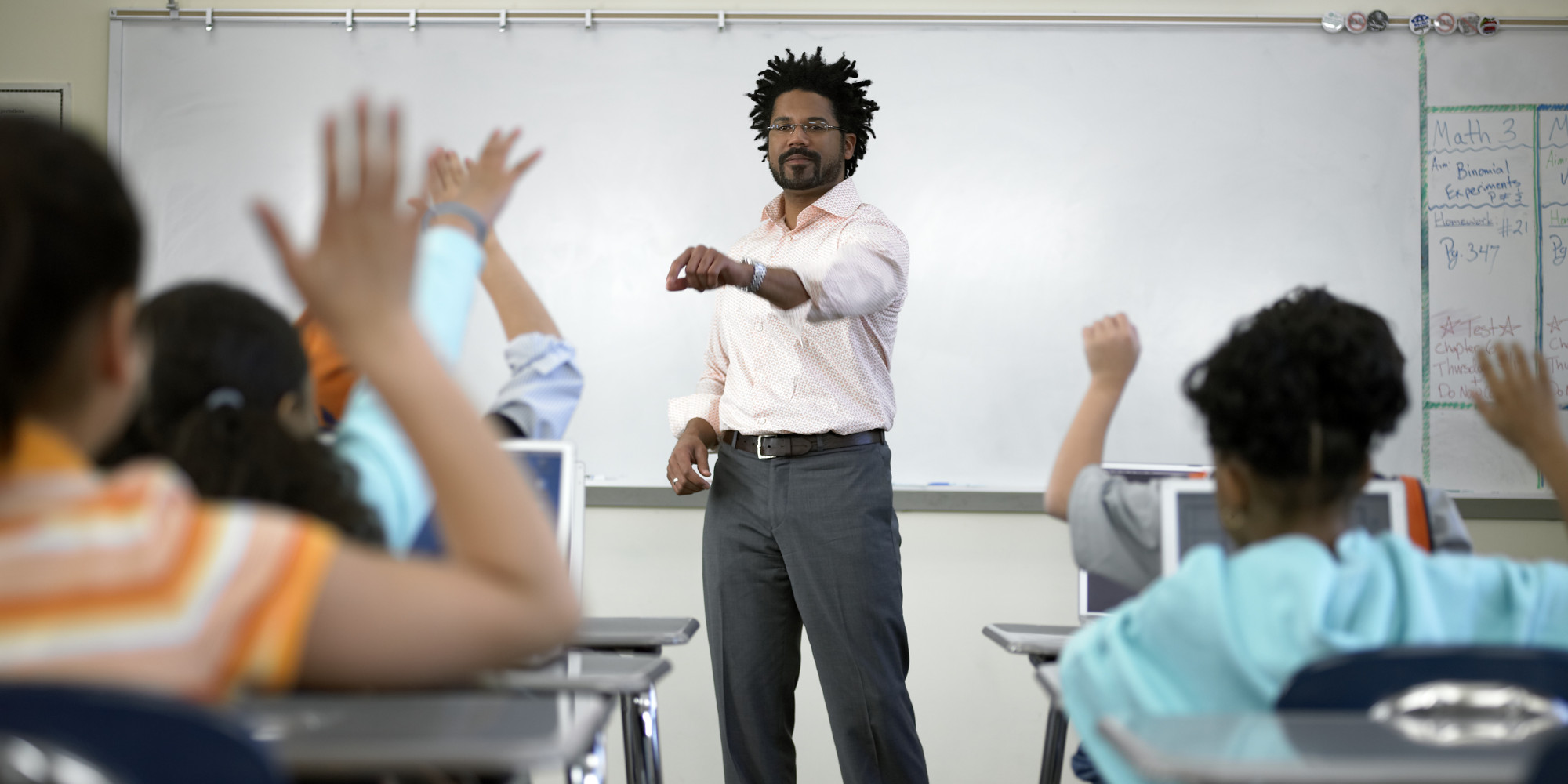 Male teacher standing before students (8-10) with hands raised